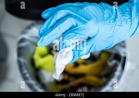 Mano nella guanto che getta via sporco salvietta igienizzante Foto Stock