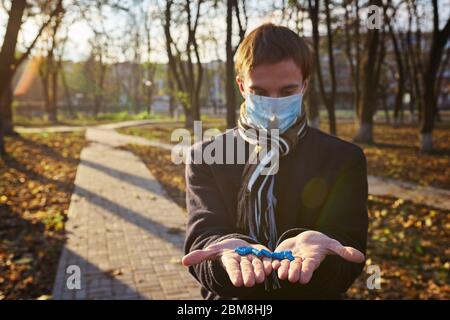 Un ragazzo in una maschera medica tiene le mani con pillole alla macchina fotografica. Foto di concetto sulla pandemia Covid 19 Foto Stock