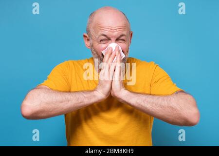 Uomo maturo in abiti gialli starnuti di essere malato su blu sfondo Foto Stock