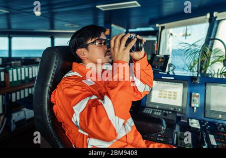 Ufficiale di ponte filippino sul ponte di nave o di nave che guarda attraverso binocoli Foto Stock