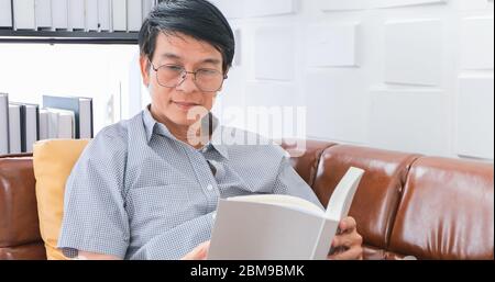 Senior Asian uomo lettura libro sul divano in soggiorno a casa, Ritratto di Asian anziani uomo è rilassante e felicità con Leggi una rivista a casa Foto Stock