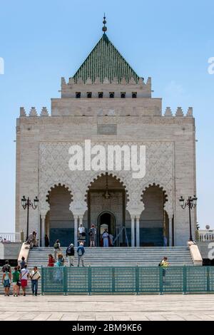 I turisti si avvicinano all'ingresso del Mausoleo di Mohammed V situato a Rabat in Marocco. Contiene le tombe del re e dei suoi due figli. Foto Stock