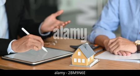 Immagine ritagliata di agente immobiliare offrire assicurazione casa o proprietà di casa per uomo intelligente in camicia blu al tavolo di legno moderno. Firma su agreeme Foto Stock