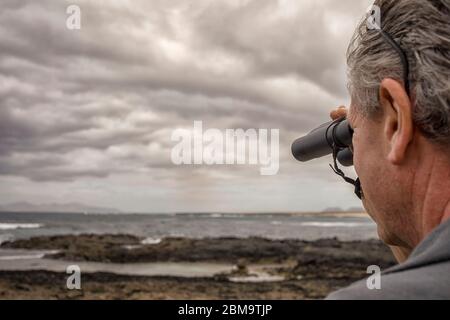 Uomo che guarda un orizzonte e oceano con il binocolo Foto Stock