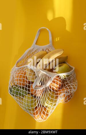 Arance, banane, mele, avocado si trovano in borsa a corda su sfondo giallo brillante e sole duro. Il concetto di zero rifiuti. Uso di sacchetti riutilizzabili in Foto Stock