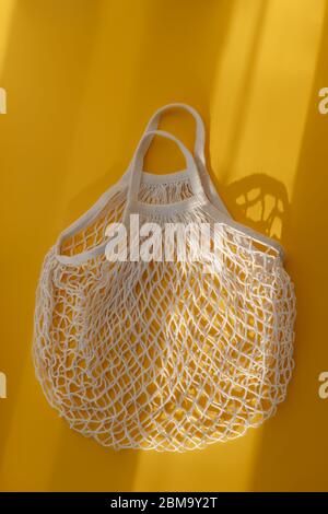 Borsa vuota a corda in rete su sfondo giallo brillante e sole duro. Il concetto di zero rifiuti. Utilizzando sacchetti riutilizzabili invece di cellofan monouso p Foto Stock