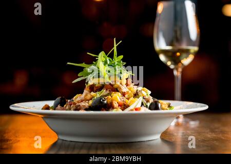 Insalata di Tun con olive, mais e rucola in tavola con un bicchiere di vino bianco Foto Stock