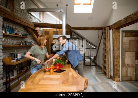 Coppia giovane amorevole che taglia insieme le verdure nella cucina rustica Foto Stock