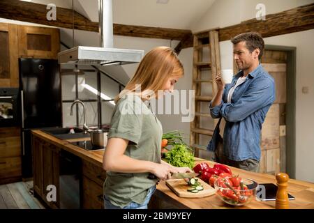 Coppia giovane amorevole che taglia insieme le verdure nella cucina rustica Foto Stock