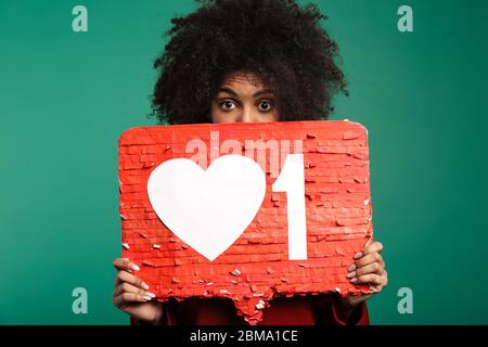 Immagine di donna riccio scioccata africana che posa isolata su sfondo muro blu scuro tenendo vuoto con simbolo simile. Foto Stock