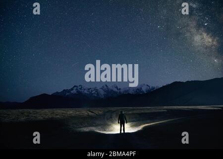 Silhouette dell uomo è la strada di illuminazione con proiettore in montagna sotto il cielo notturno con le stelle. Foto Stock