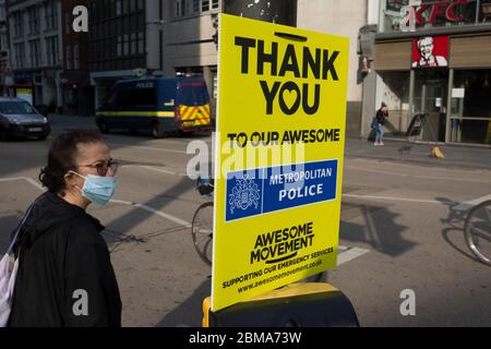 Con il blocco di Coronavirus che continua nel fine settimana festivo della Banca, quando il primo ministro Boris Johnson è tenuto a dire alla nazione che solo un graduale allentamento delle norme e delle regole di distanza sociale devono ancora essere in atto, Una persona che indossa una maschera chirurgica si prepara a attraversare Bishopsgate dove un cartello che sostiene i lavoratori dei servizi di emergenza come la polizia è stato attaccato ad un posto di attraversamento nella City of London, il distretto finanziario della capitale, il 7 maggio 2020, a Londra, Inghilterra. Foto Stock