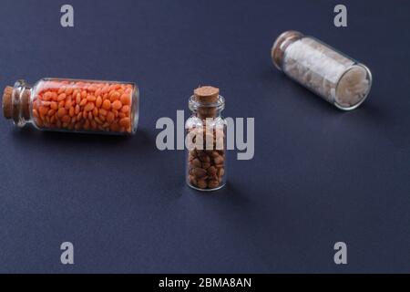 Mini bottiglie in vetro trasparente con coperchi in sughero marrone chiusi riempiti di grani non cotti. Foto Stock