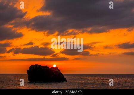 Colori incredibili nel cielo nuvoloso. Tramonto su una roccia solitaria in un mare tranquillo Foto Stock