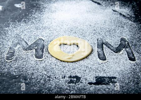 Mather Day. Word Mum che si fa dalla farina e l'impasto su sfondo scuro. Viste dall'alto, primo piano Foto Stock