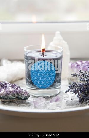 Candela di vetro bruciante con segno fatto in casa che mostra simbolo di Fiore della vita in casa interni con semi-preziose pietre geodes. Simboli spirituali in casa. Foto Stock