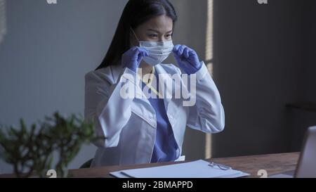 Medico che lavora al computer. L'operatore medico grazioso corracts la maschera medica quando conduce la ricerca del calcolatore nel campo della medicina. Ricerca medica Foto Stock