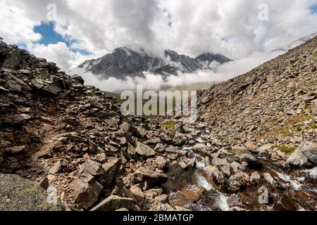 Piccolo fiume che scorre tra le pietre in montagna. Molte pietre sulle pendici delle montagne. In lontananza, una montagna nascosta dalle nuvole. Orizzonte Foto Stock