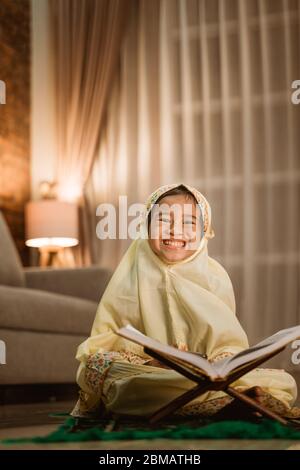 felice ragazzo musulmano sorridente mentre legge quran a casa Foto Stock