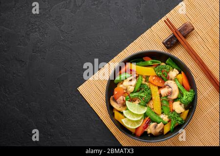 Pad Pak Ruam o verdure Tailandese fritte Stir-in ciotola nera su sfondo ardesia scuro. Pad Pak è cucina tailandese piatto vegetariano con mix di verdure Foto Stock