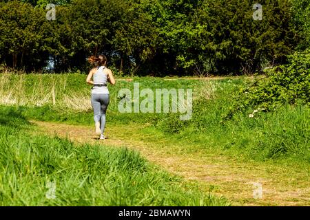 Donna che fa jogging lungo un percorso verde nelle paludi di Hackney, Londra Foto Stock