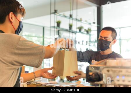 Cameriere concettuale a distanza sociale che offre al cliente una borsa da asporto al bar. Foto Stock