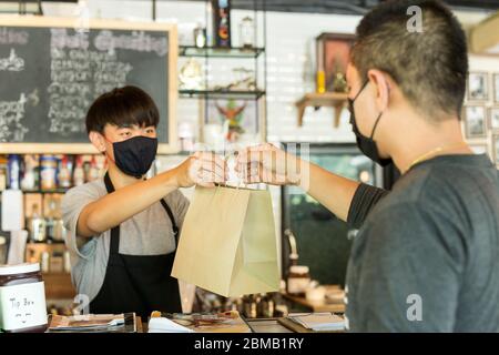 Cameriere concettuale a distanza sociale che offre al cliente una borsa da asporto al bar. Foto Stock