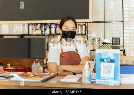 Donna proprietario caffè che indossa maschera protettiva stand in contatore Covid-19 concettuale. Foto Stock