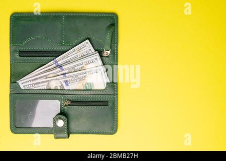 Diverse centinaia di banconote da dollaro sporgono da un elegante portafoglio in pelle verde su uno sfondo giallo brillante. Vista dall'alto con spazio libero Foto Stock