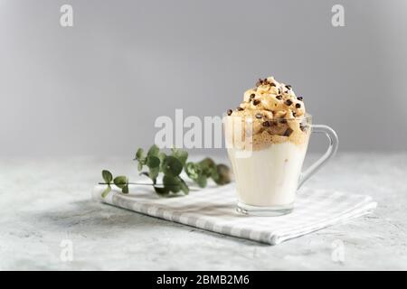 Dalgona in una tazza di vetro trasparente decorata con gocce di cioccolato, bevanda coreana di tendenza fatta con latte e schiuma di caffè su sfondo grigio Foto Stock