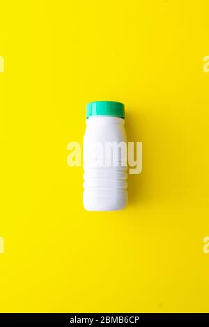 Flacone di plastica bianco con tappo verde su sfondo giallo situato al centro. Riciclare la plastica nel contenitore giallo Foto Stock