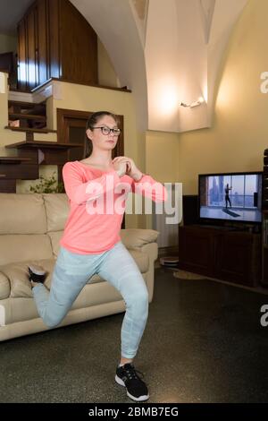 La ragazza giovane sta facendo l'esercitazione di affondo nella stanza a casa. Allenamento femminile per mantenersi in forma e in forma. Concetto di cura di sé a casa e a casa workou Foto Stock