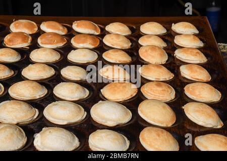 Tipici poffertjes olandesi - piccole frittelle-essendo cotte su una pentola pesante di ferro in preparazione durante il festival di cibo di strada, un evento all'aperto, traditiona Foto Stock