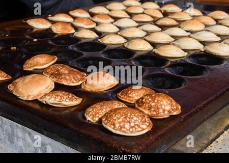 Tipici poffertjes olandesi - piccole frittelle-essendo cotte su una pentola pesante di ferro in preparazione durante il festival di cibo di strada, un evento all'aperto, traditiona Foto Stock