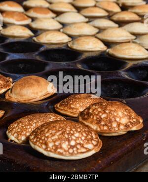 Tipici poffertjes olandesi - piccole frittelle-essendo cotte su una pentola pesante di ferro in preparazione durante il festival di cibo di strada, un evento all'aperto, traditiona Foto Stock