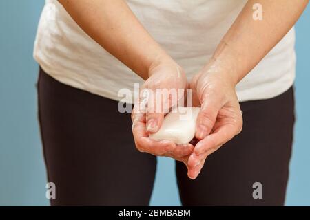 Donna lavando le mani con sapone su sfondo blu. La pulizia corretta delle mani protegge dalle infezioni. Concetto di igiene e pulizia. Foto Stock