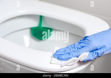 Pulire con guanti chirurgici il contenitore del water con salviette disinfettanti bagnate. Prevenzione della diffusione di batteri e coronavirus . Foto Stock