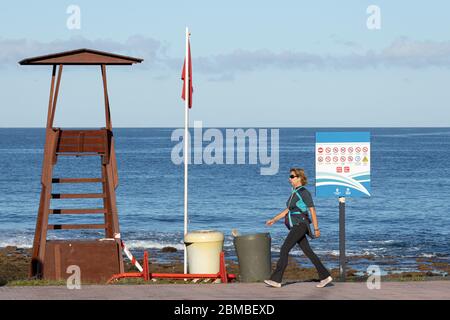 La Caleta, Costa Adeje, Tenerife, Isole Canarie, Spagna. 8 maggio 2020. Donna che si batte in una veloce passeggiata sul lungomare durante il tempo assegnato per l'esercizio durante la fase 0 del piano di de-escalation dello Stato di emergenza per Covid 19, Coronavirus, lungo la costa, oltre una torre bagnino su Playa Enramada, Adeje Foto Stock