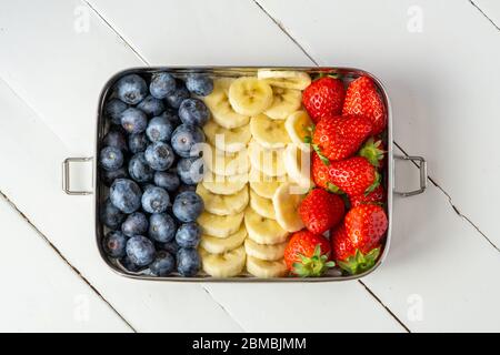 Mirtilli, banane e fragole in un grande contenitore di alimenti in acciaio inossidabile. Pranzo in plastica senza scatola isolato su sfondo bianco. Zero rifiuti, Foto Stock