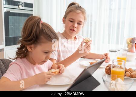 Due sorelle che hanno colazione e guardare i cartoni animati su tablet insieme, felice concetto di famiglia Foto Stock