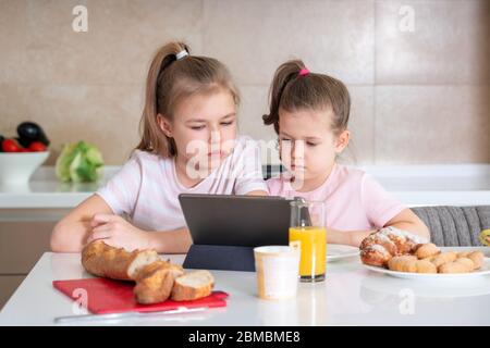 Due sorelle che hanno colazione e guardare i cartoni animati su tablet insieme, felice concetto di famiglia Foto Stock