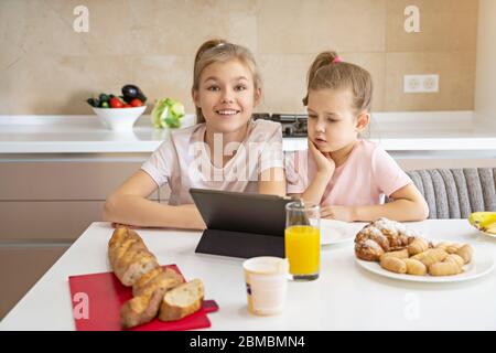 Due sorelle che hanno colazione e guardare i cartoni animati su tablet insieme, felice concetto di famiglia Foto Stock