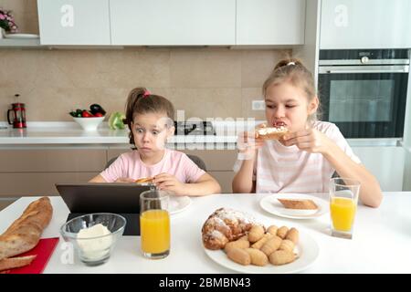 Due sorelle che hanno colazione e guardare i cartoni animati su tablet insieme, felice concetto di famiglia Foto Stock