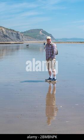 Charmouth Dorset, Regno Unito. 8 maggio 2020. UK Weather: Un pomeriggio caldo e soleggiato in riva al mare a Charmouth, West Dorset. Nonostante il bel tempo le spiagge rimangono tranquille sul 75 ° aniverario del giorno VE come la gente continua a seguire i consigli per rimanere a casa durante il blocco pandemico coronavirus. Un uomo cammina sulla spiaggia deserta. Credit: Celia McMahon/Alamy Live News Foto Stock