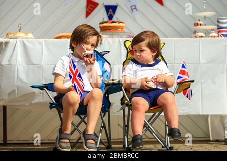 Halesowen, West Midlands, Regno Unito. 8 maggio 2020. I fratelli Zachary (4) e Hugo (2) Hickin godono di una torta a tema del VE Day 75, ognuno dei quali siede nel loro viaggio di fronte ad Halesowen, West Midlands. Credit: Peter Lopeman/Alamy Live News Foto Stock