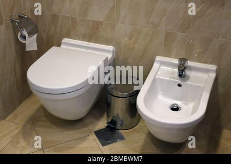 Bagno / toilette / wc / WC con sedili wc, carta igienica e una bidone di rifiuti. Lussuosa porcellana bianca e piastrelle marroni. Foto Stock