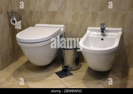 Bagno / toilette / wc / WC con sedili wc, carta igienica e una bidone di rifiuti. Lussuosa porcellana bianca e piastrelle marroni. Foto Stock