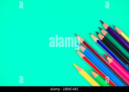 Molti pastelli di matita di legno di colore diverso messi sulla parte superiore di uno sfondo di carta blu chiaro Foto Stock