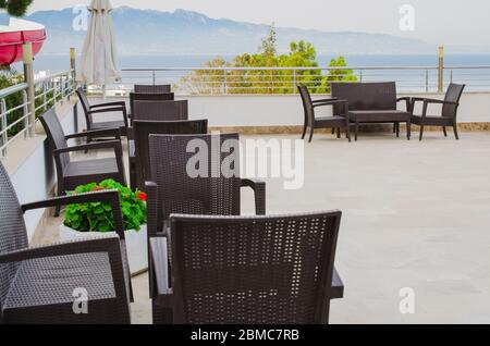 Tavoli e sedie in vimini sulla terrazza di un accogliente caffè estivo. Foto Stock