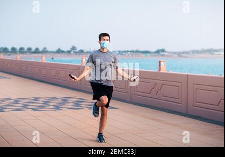 Uomo che si esercita con una corda di salto e indossa una maschera chirurgica protettiva all'aperto Foto Stock